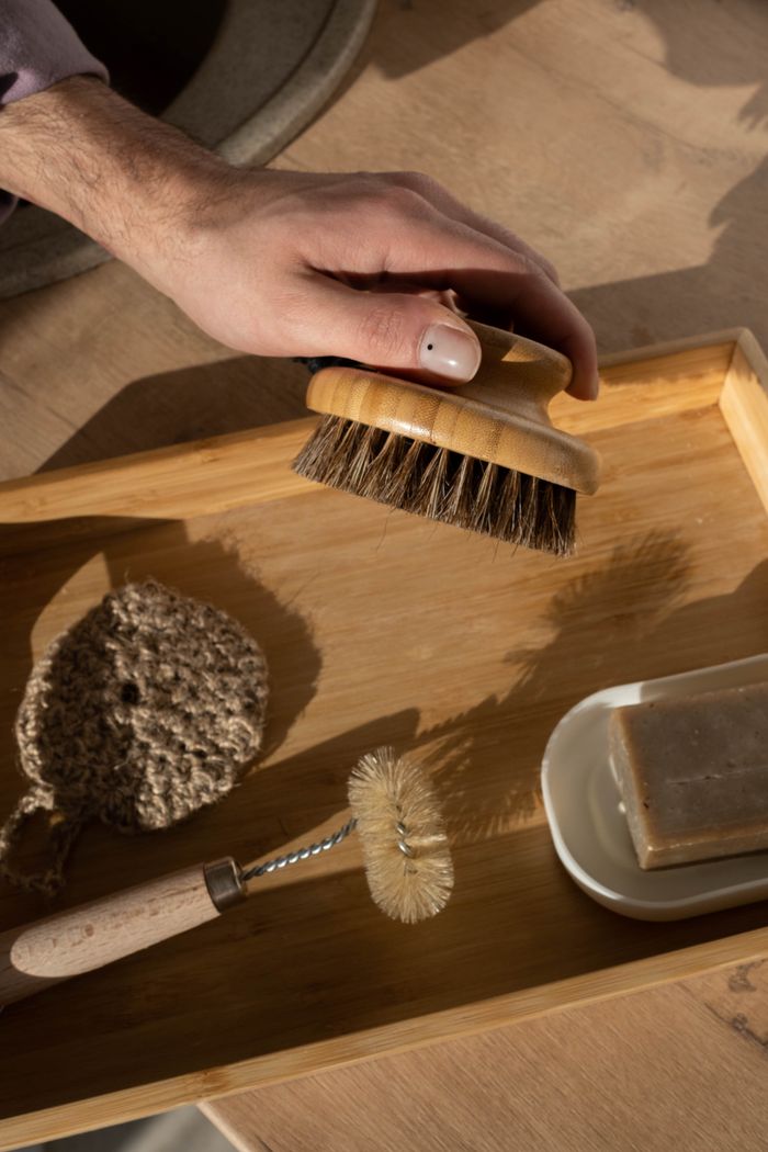 project-01-b Close-up of hand holding a wooden brush on a bamboo tray with cleaning tools.